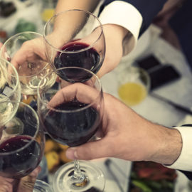 Top-down view of male and female hands with filled glasses of wine above the restaurant tabletop. Drinking toasts and clinking tumblers at a dinner party. Drinking wine at a banquet. Feast an event